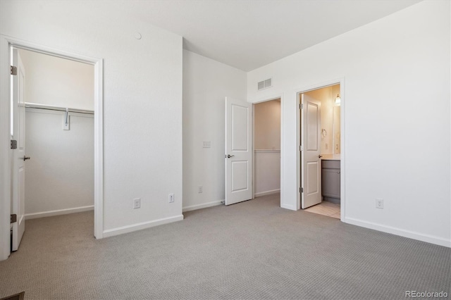 unfurnished bedroom with light colored carpet, a spacious closet, connected bathroom, and a closet