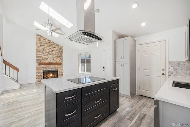 kitchen featuring black electric stovetop, island range hood, light countertops, dark cabinets, and light wood-style flooring