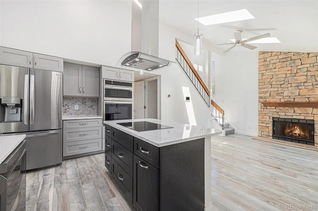 kitchen featuring a skylight, gray cabinetry, high vaulted ceiling, ventilation hood, and stainless steel appliances