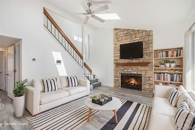 living room featuring a stone fireplace, ceiling fan, wood finished floors, and stairway