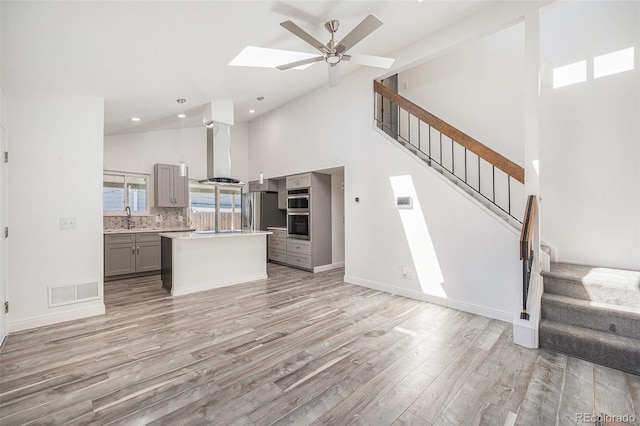 unfurnished living room featuring stairs, visible vents, a sink, and light wood-style floors