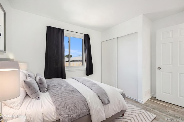 bedroom with light wood-type flooring, baseboards, visible vents, and a closet