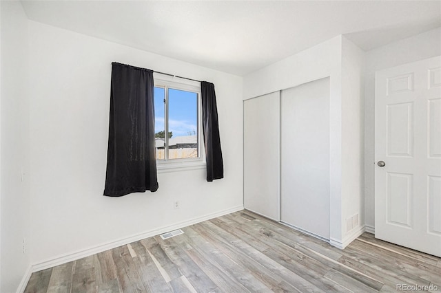 unfurnished bedroom with baseboards, visible vents, wood finished floors, and a closet