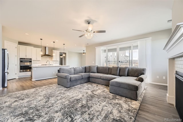 living room featuring a tiled fireplace, ceiling fan, sink, and light hardwood / wood-style floors