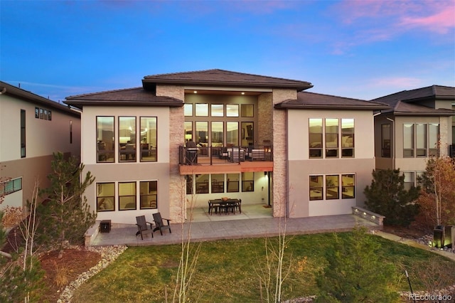 back house at dusk featuring a patio area and a yard