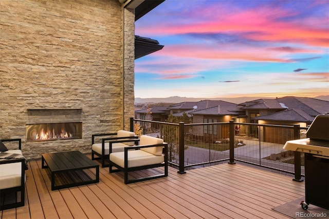 deck at dusk with an outdoor living space with a fireplace and a grill