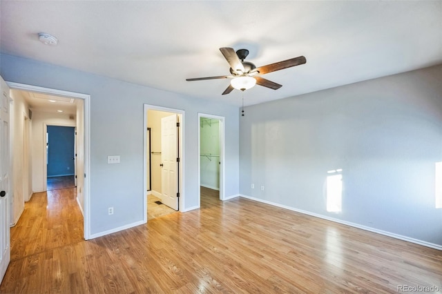 unfurnished bedroom with a closet, a spacious closet, light wood-style floors, ceiling fan, and baseboards