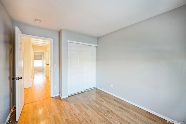 unfurnished bedroom featuring light wood-type flooring, a closet, and baseboards