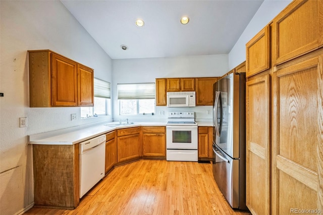 kitchen with white appliances, a sink, light countertops, light wood finished floors, and brown cabinetry