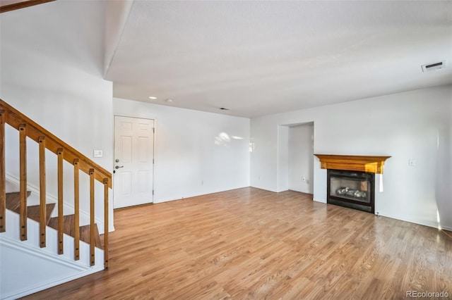 unfurnished living room featuring stairs, visible vents, a fireplace, and wood finished floors