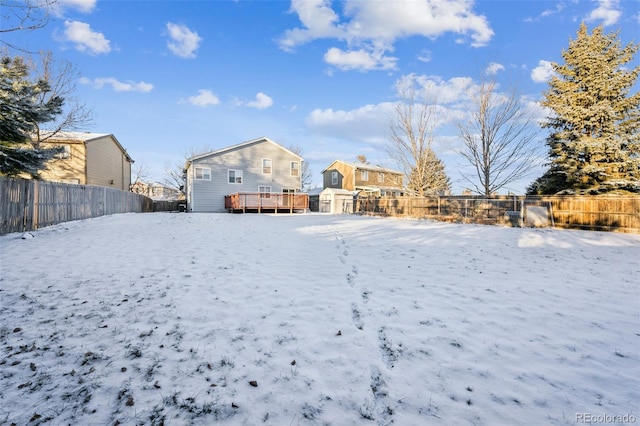 yard layered in snow featuring a storage shed, a fenced backyard, a deck, and an outbuilding