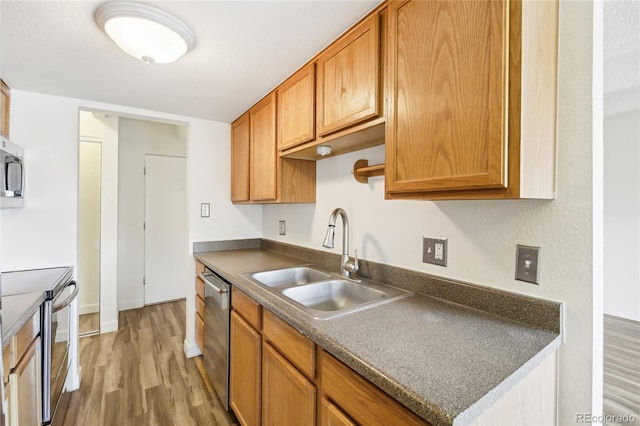 kitchen with light wood-style floors, a sink, dark countertops, and stainless steel appliances