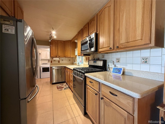 21300 County Road 13, La Jara, CO 81140 - kitchen featuring brown cabinets, light tile patterned flooring, tasteful backsplash, appliances with stainless steel finishes, and washer / clothes dryer