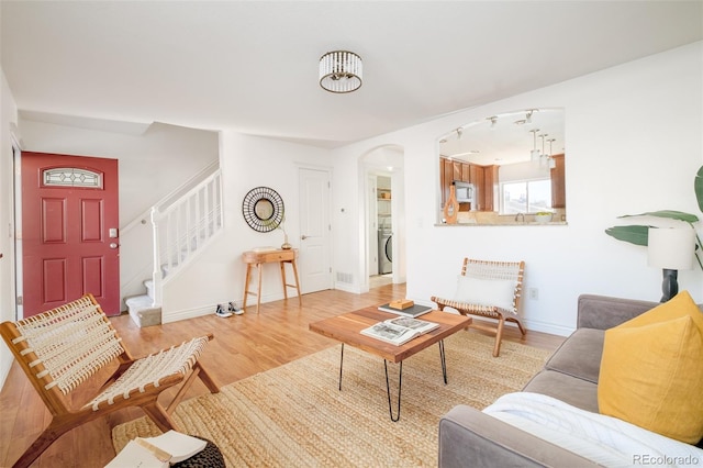 living room featuring rail lighting, washer / dryer, and light hardwood / wood-style flooring