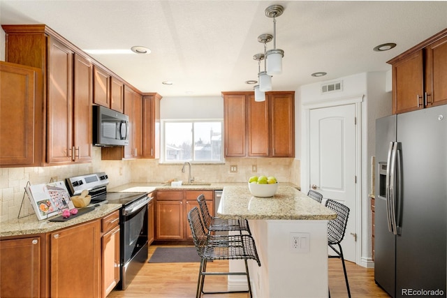 kitchen featuring stainless steel appliances, light stone countertops, hanging light fixtures, and a breakfast bar