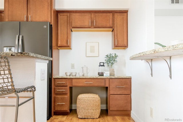 kitchen with stainless steel refrigerator, light stone countertops, and light wood-type flooring