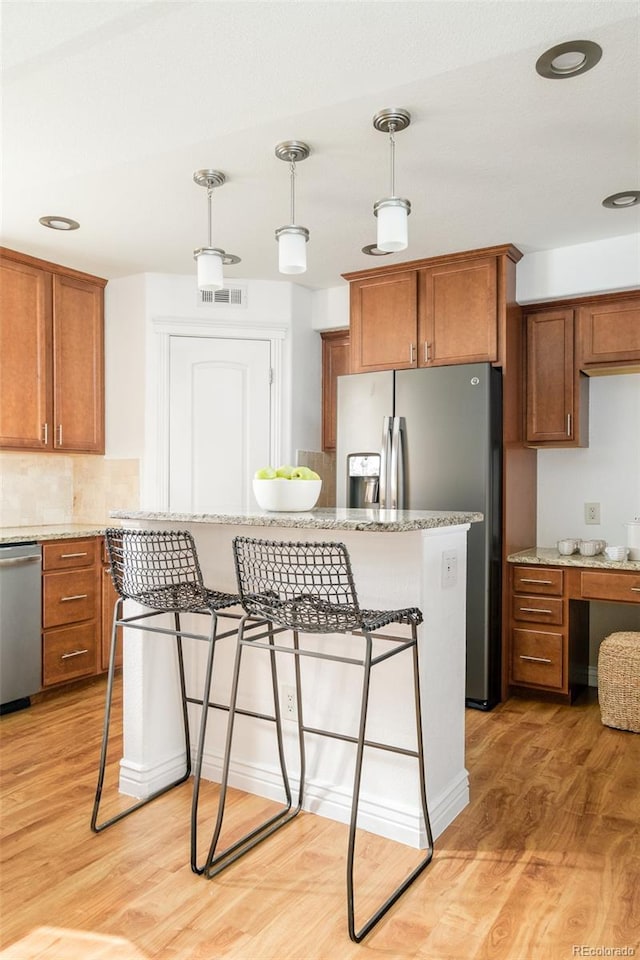 kitchen with decorative light fixtures, light wood-type flooring, a kitchen breakfast bar, and appliances with stainless steel finishes