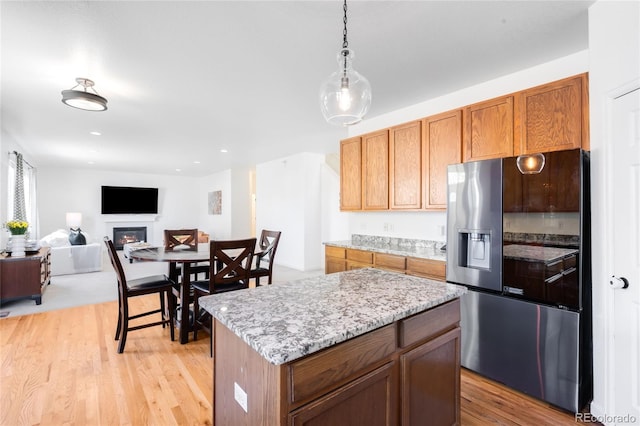 5861 Mt Shadows Blvd, Firestone, CO 80504 - kitchen with stainless steel refrigerator with ice dispenser, light wood finished floors, a warm lit fireplace, decorative light fixtures, and a kitchen island