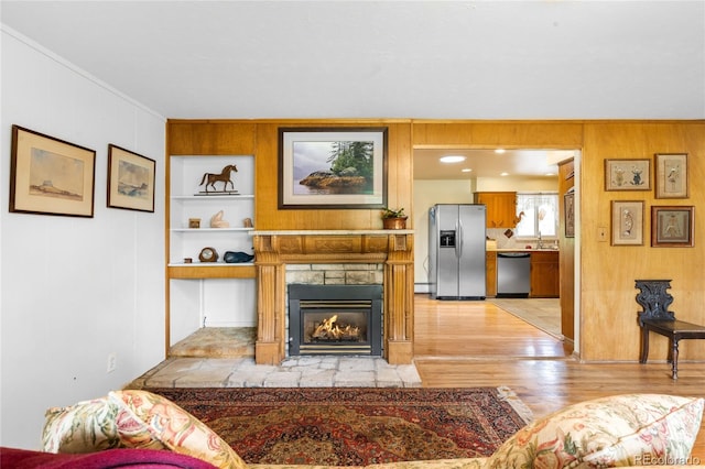 9045 W Ithaca Pl, Denver, CO 80235 - living area with light wood-style flooring, crown molding, a stone fireplace, wooden walls, and a baseboard radiator