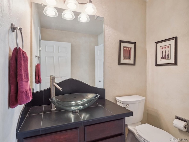 bathroom featuring a textured wall, toilet, and vanity