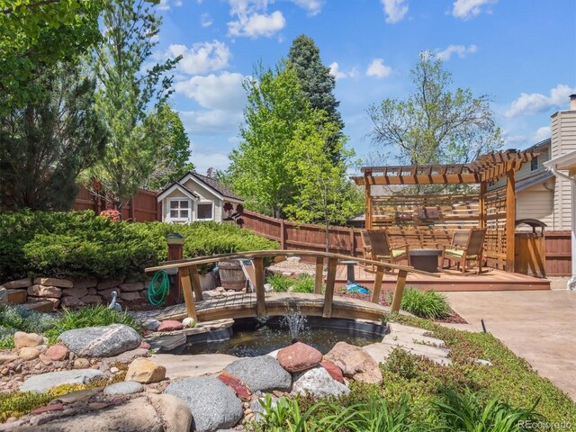 view of yard featuring a deck, fence, a garden pond, and a pergola