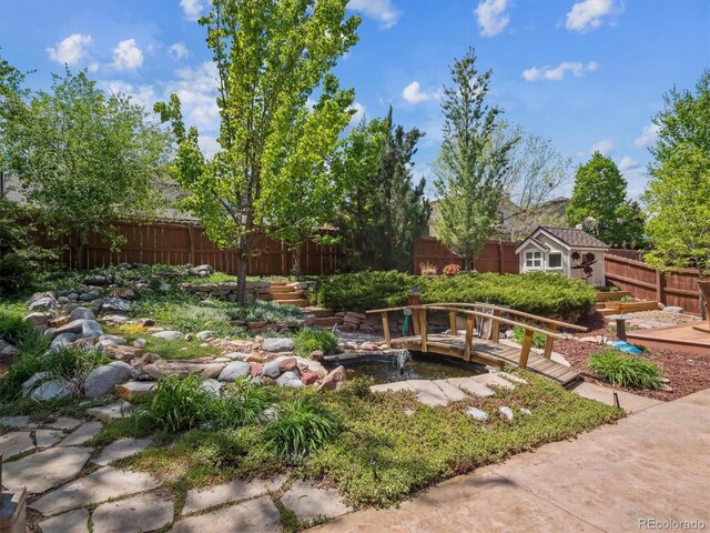 fenced backyard with an outdoor structure, a storage unit, and a small pond