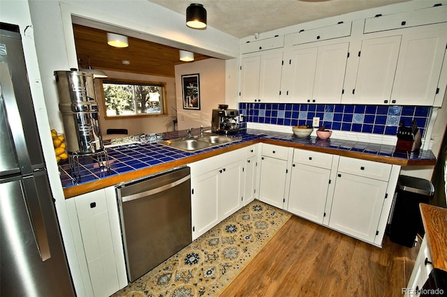 kitchen with appliances with stainless steel finishes, dark hardwood / wood-style flooring, sink, white cabinets, and tile counters