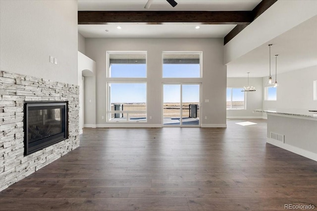 unfurnished living room featuring dark hardwood / wood-style flooring, ceiling fan with notable chandelier, a fireplace, and beamed ceiling