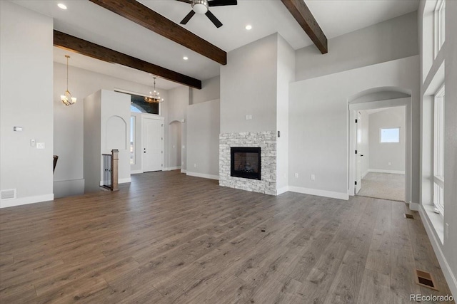 unfurnished living room featuring a towering ceiling, ceiling fan with notable chandelier, a fireplace, beamed ceiling, and dark wood-type flooring