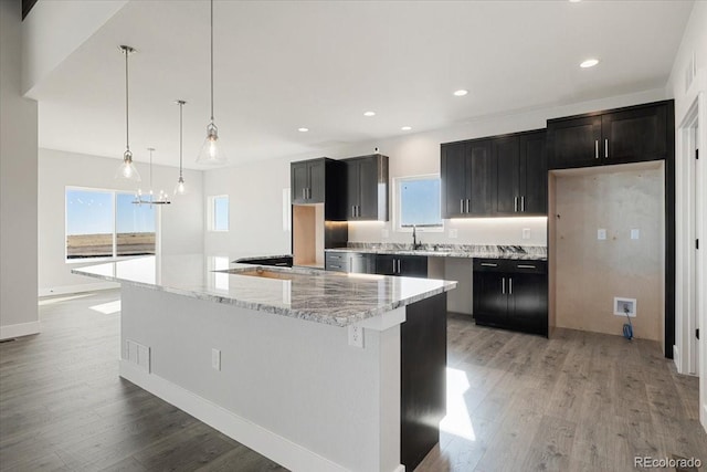 kitchen with sink, light stone counters, decorative light fixtures, light hardwood / wood-style flooring, and a large island