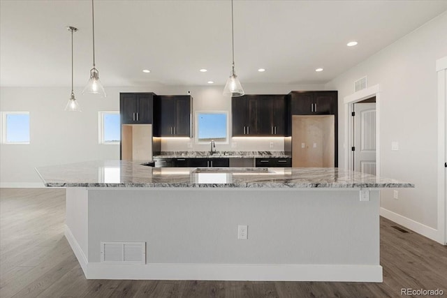 kitchen featuring hanging light fixtures, fridge, a large island, light stone countertops, and hardwood / wood-style floors