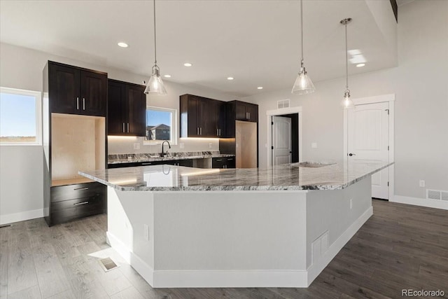 kitchen featuring a large island, decorative light fixtures, dark brown cabinets, and wood-type flooring