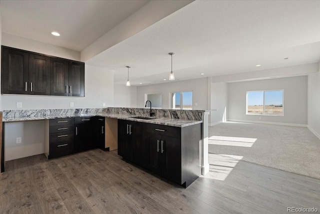 kitchen featuring sink, hanging light fixtures, kitchen peninsula, light stone countertops, and light hardwood / wood-style flooring