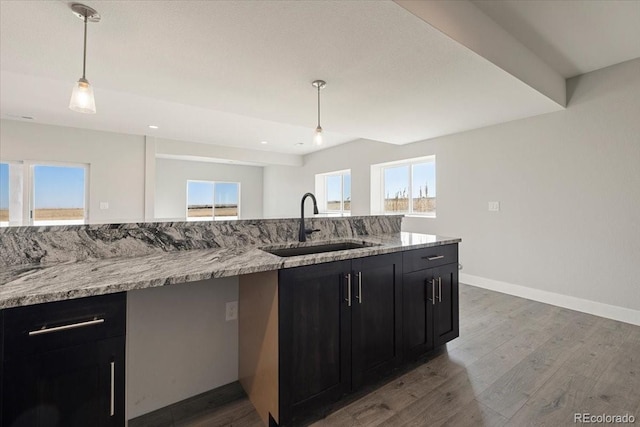 kitchen featuring sink, dark wood-type flooring, light stone counters, and decorative light fixtures