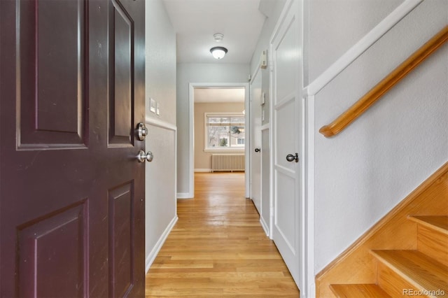 corridor featuring light wood-style floors, baseboards, and radiator