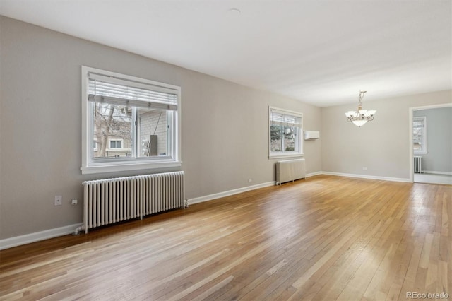 empty room featuring a notable chandelier, light wood-style flooring, radiator, and radiator heating unit