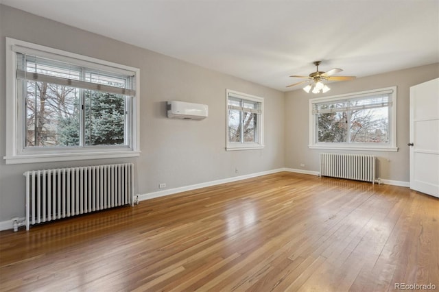 empty room with a wall mounted air conditioner, radiator, light wood-style flooring, and a ceiling fan