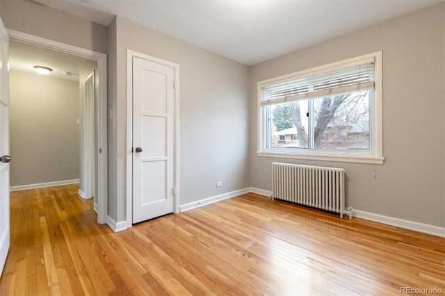 unfurnished bedroom featuring radiator, baseboards, and light wood-type flooring