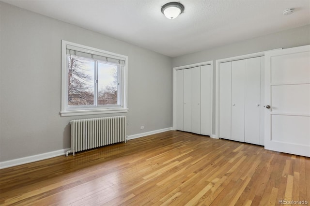 unfurnished bedroom featuring light wood-style flooring, radiator heating unit, baseboards, and two closets