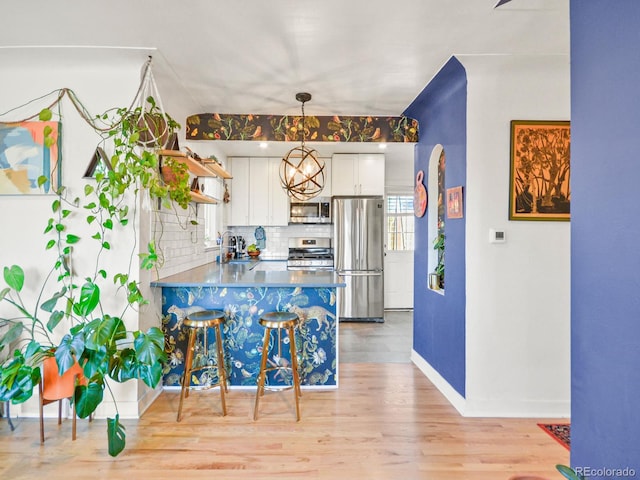 3450 N Harrison St, Denver, CO 80205 - kitchen featuring a peninsula, light wood-style flooring, decorative backsplash, white cabinets, and appliances with stainless steel finishes