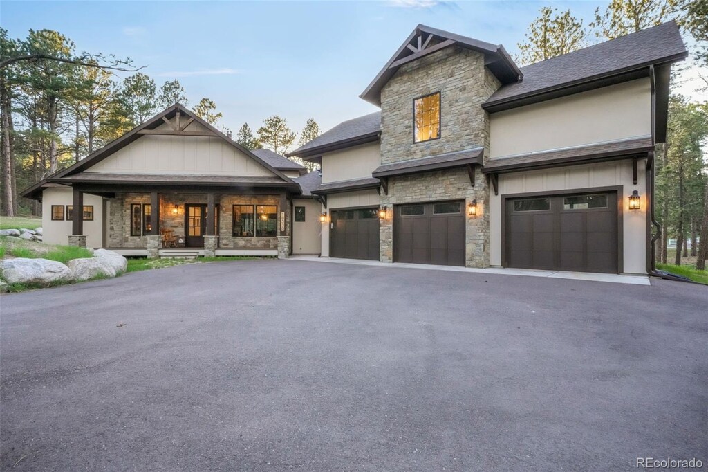 18330 Archers Dr, Monument, CO 80132 - view of front facade with stone siding, covered porch, asphalt driveway, an attached garage, and stucco siding