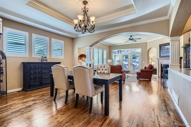 dining room featuring arched walkways, a raised ceiling, a glass covered fireplace, and wood finished floors