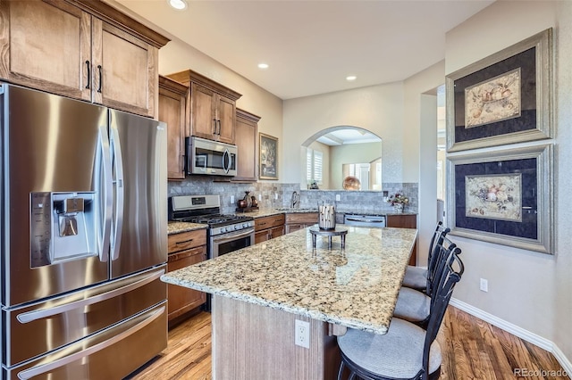 kitchen featuring a center island, a breakfast bar area, decorative backsplash, appliances with stainless steel finishes, and light stone countertops