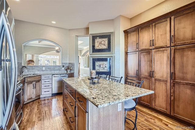 kitchen with stainless steel appliances, a sink, wood finished floors, a kitchen island, and a kitchen breakfast bar