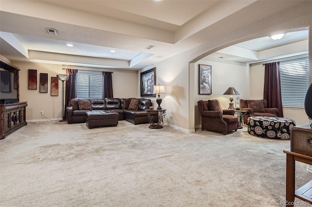 carpeted living room featuring baseboards, visible vents, a raised ceiling, and arched walkways