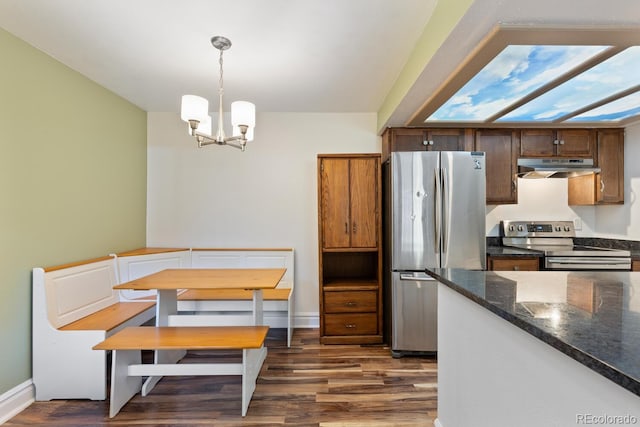 kitchen with dark wood-type flooring, decorative light fixtures, an inviting chandelier, stainless steel appliances, and under cabinet range hood