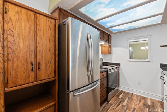 kitchen with under cabinet range hood, stainless steel appliances, dark wood-type flooring, brown cabinets, and dark countertops