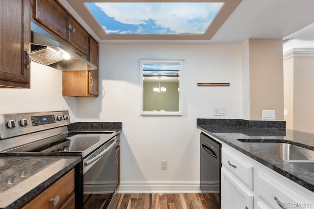 kitchen with under cabinet range hood, wood finished floors, black dishwasher, dark stone counters, and stainless steel range with electric stovetop