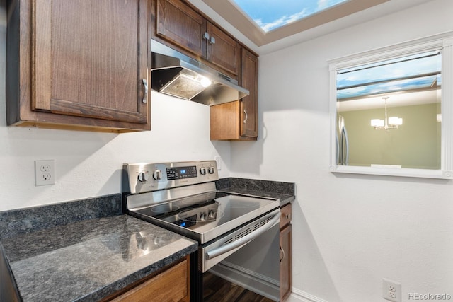 kitchen featuring stainless steel appliances, brown cabinetry, dark stone countertops, a chandelier, and under cabinet range hood