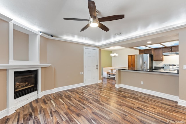 unfurnished living room with baseboards, visible vents, a glass covered fireplace, dark wood-style flooring, and ceiling fan with notable chandelier